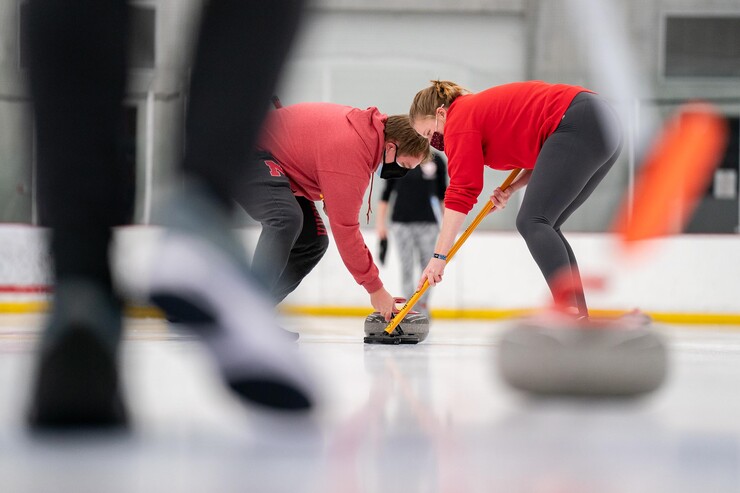 Two curlers sweep the ice in front of the stone.