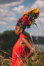 Jazzmeia Horn standing in field wearing red dress and flower headdress