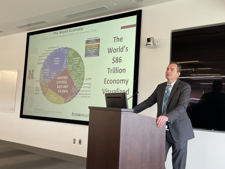 Matthew Schaefer, Clayton Yeutter Chair in the University of Nebraska College of Law, stands at a lecturn next to a screen with a multicolored chart and the words "The world's $86 trillion economy visualized."