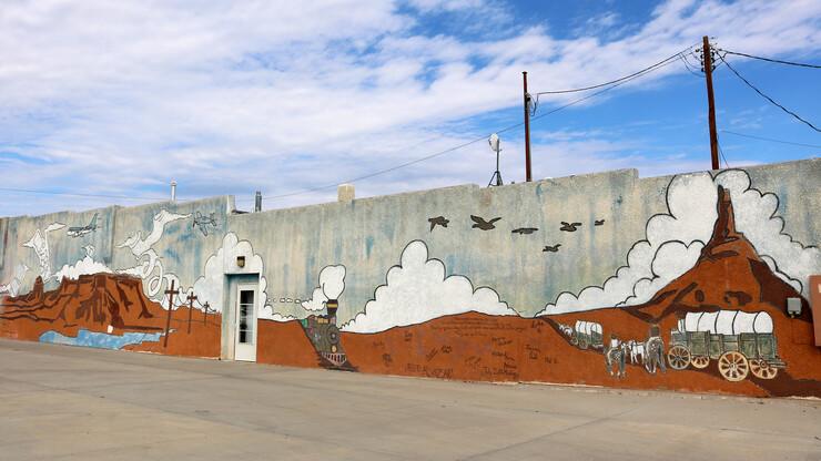 A mural of the landscape near Scottsbluff featuring Courthouse Rock and Chimney Rock, with planes flying overhead, a locomotive and a wagon train.