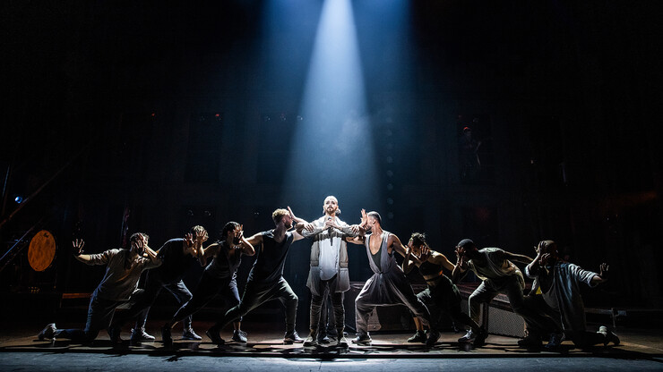 A "Jesus Christ Superstar" cast member stands in a spotlight, with four people striking poses on each side.