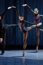 Three ballet dancers — two women and a man — stand on their tiptoes.