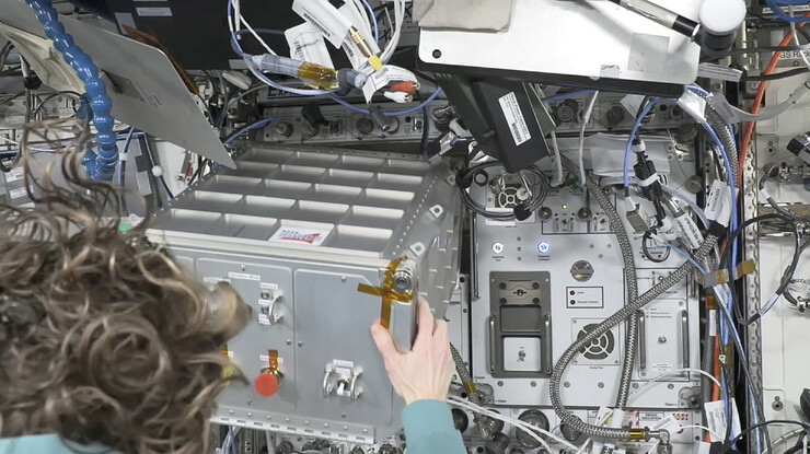Astronaut Loral O’Hara pulls out a silver box from a wall of instruments.