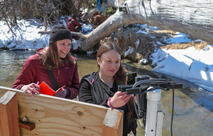 Mary Harner and Jamila Bajelan look at a camera near a creek.