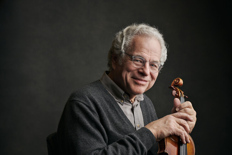 Itzhak Perlman poses with his violin in a dark room.