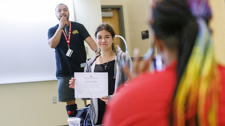 Jocelyn Cabellos, a freshman at Omaha South Magnet School, holds her academy certificate for a photo as David Orozco-Garcia, an NCPA counselor for Omaha South calls up the next student.