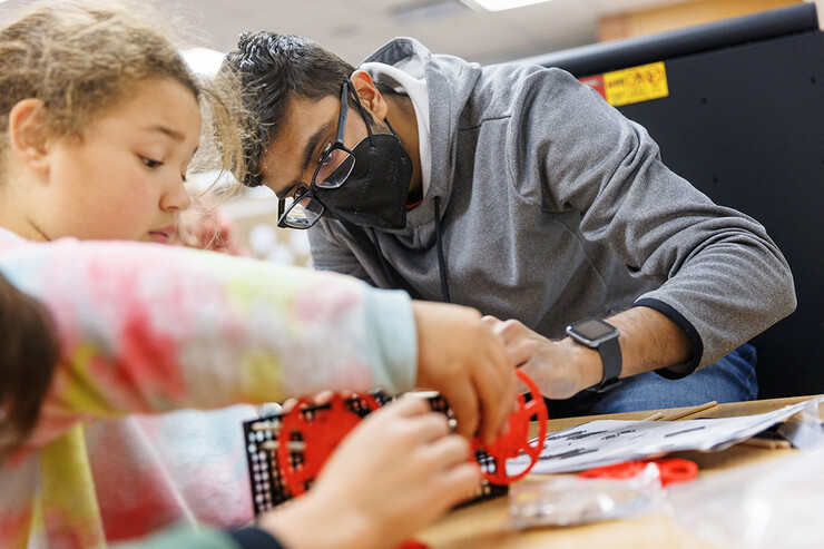 Rohan Tatineni helps a student build her rubber-band powered car. 