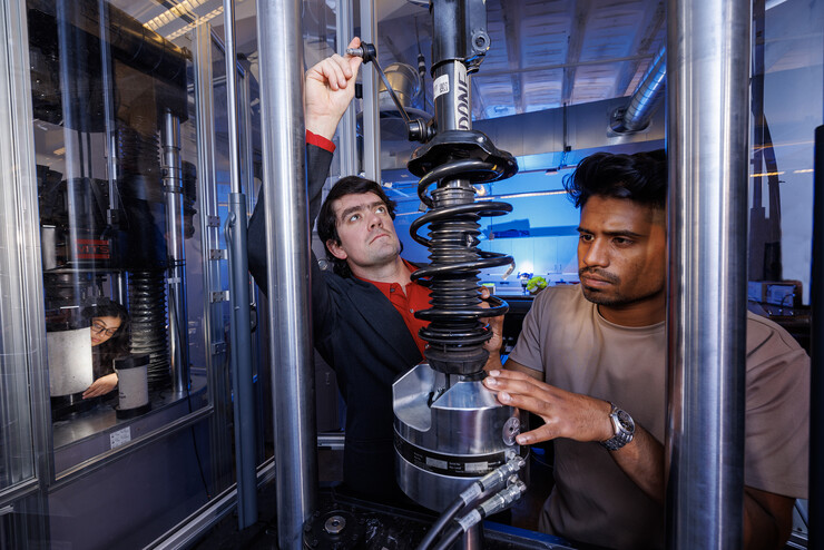 Cody Stolle (center) evaluates small car suspension components in a load frame with students Gnyarienn Selva Kumar (right) and Mahfuza Rahman (left).