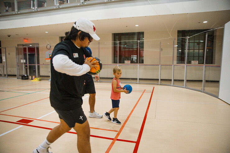 An Itty Bitty Sports coach works with a participant on passing a basketball.
