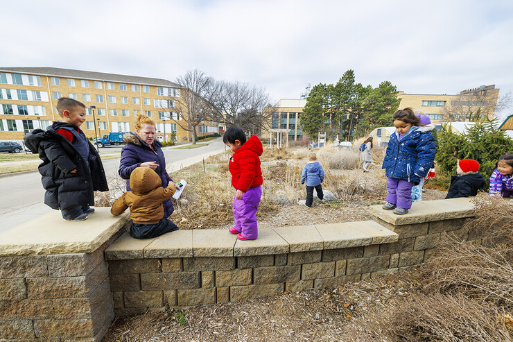 Madeline Williams helps the children as they walk along a low stone wall in the Backyard Farmer Garden.