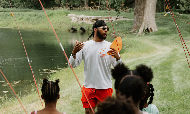 Elijah Riley standing outside providing youth information on how to fish.