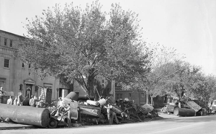 Students walk through scrap items collected outside of a Greek house during a scrap collection drive held as part of homecoming activities in 1942.