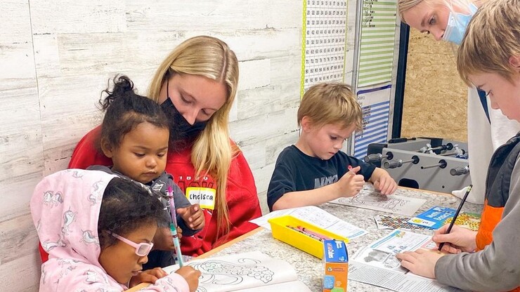 A member of Alpha Xi Delta sits with a child on her lap as they draw in a coloring book. 