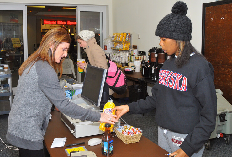Jill Morris (left), a sales clerk with the Nebraska Unions, rings up a sale inside the Rotunda Gallery in the Nebraska Union. The welcome desk and Caffina Café have been temporarily moved into the gallery space on the east side of the north entrance. (© 2013, The Board of Regents of the University of Nebraska. All rights reserved.)