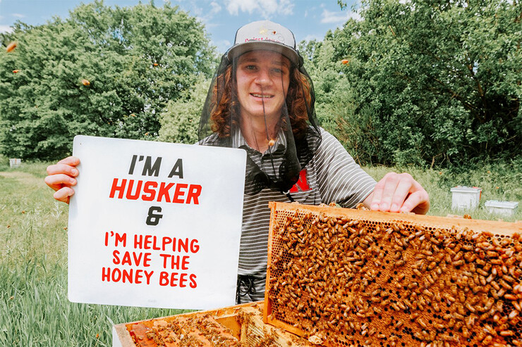 Rogan Tokach holds a sign that reads "I'm a Husker & I'm helping save the honey bees"