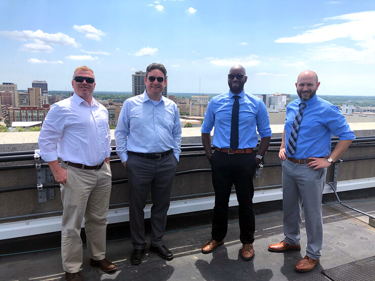 Grant team on a rooftop in downtown Lincoln, Nebraska, to view one of several city-wide testbeds the CPN Lab uses to facilitate research in dynamic spectrum access, 5G, vehicular networks, underground wireless communications and radio frequency machine learning. From left: Bryan Woosley, NSWC university liaison; Mehmet Can Vuran, CPN Lab director; James Stewart, NSWC chief scientist; Jonny Axton, NSWC electronics engineer.