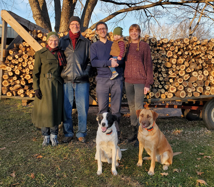 Amber Reinkordt with her husband, baby, in-laws and dogs. The family is standing in front of a stack of Eastern Red Cedar cleared from their land.
