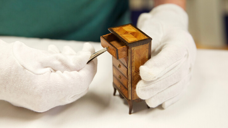 DiAnna Hemsath uses tweezers to open the drawer on one of the miniatures in the Kruger collection. This handcrafted piece includes wood inlay and custom cast bronze drawer pulls.
