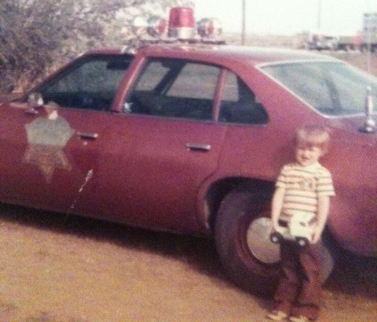 A very young Troy Fedderson standing next to his father's Brown County, South Dakota, deputy sheriff patrol car.