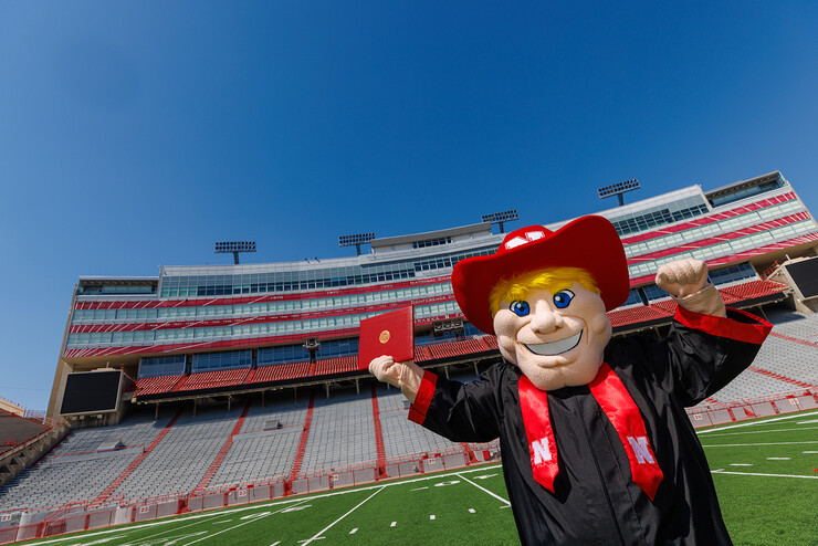 Herbie Husker holds a diploma on the field at Memorial Stadium.