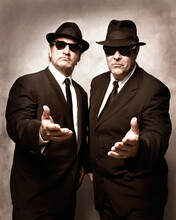 Jim Belushi and Dan Aykroyd, wearing suits with sunglasses and black fedoras