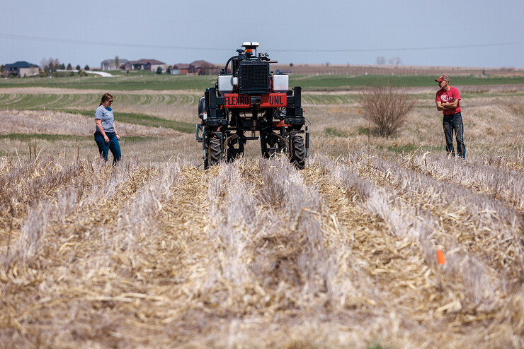A man and a woman walk behind the Flex-Ro autonomous planting robot in a field.