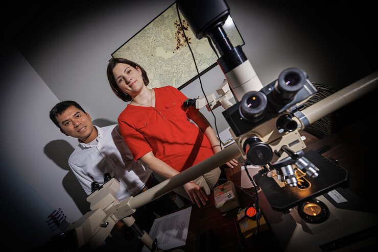 Husker scientists Hiep Vu and Sarah Sillman stand in a shadowy room, with a microscope in the foreground.