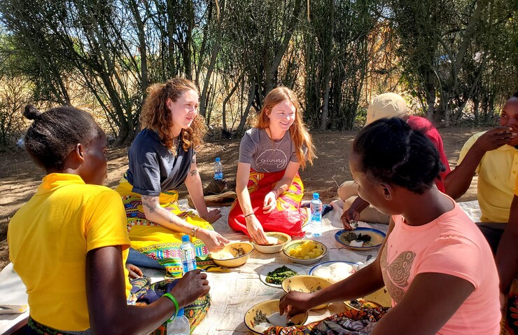 Claire Gillespie and Katie Schmitz dine with Zambians on a blanket.