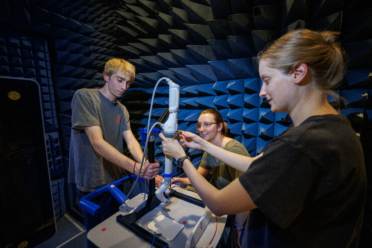 Sean Crimmins, Erika Smith and Rachael Wagner adjust the robotic arm on a stand in a chamber for electromagnetic compatibility and electromagnetic interference testing.