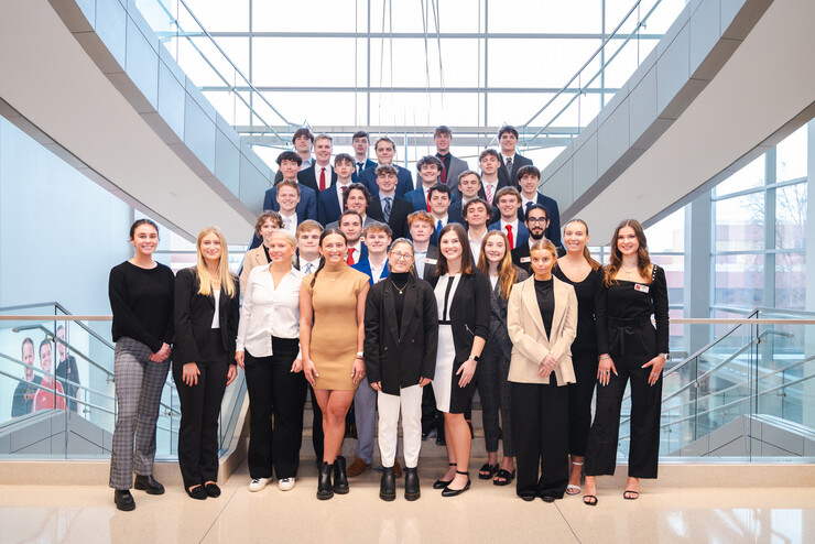 Thirty-four students in business attire pose on a staircase in Hawks Hall.