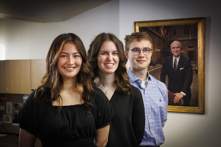 Husker undergraduates Kyoko Wall, Victoria Diersen and Zane Mrozla-Mindrup stand in front of a framed portrait of Clayton Yeutter.