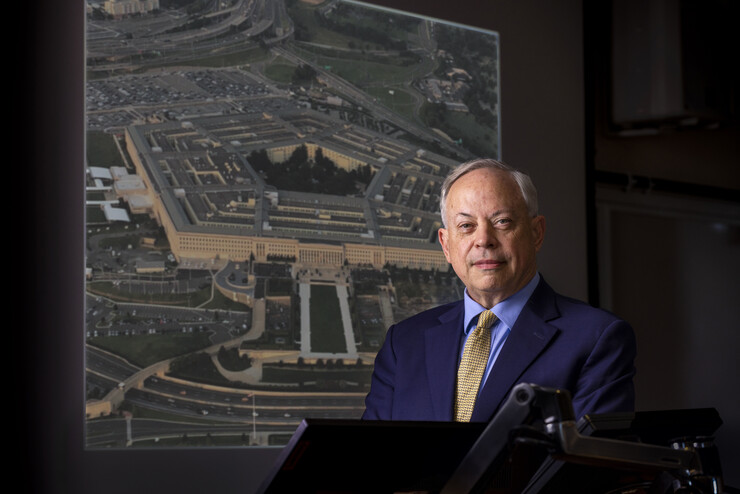 Jack Beard in a dark room, with a photo of the Pentagon in the background