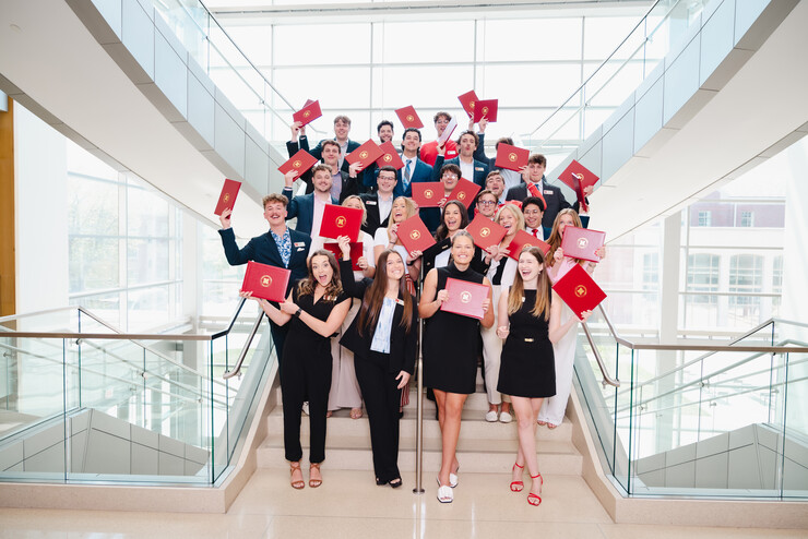About two dozen university students pose on a staircase with their certificates of sales excellence.