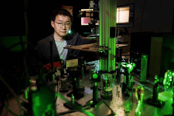 Yinsheng Guo stands over an array of instruments, glowing green in a dark room.