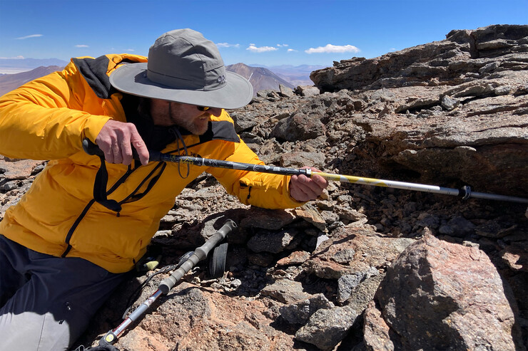 Jay Storz uses a walking stick to probe beneath rocks for mummified mice