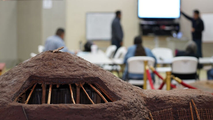 A replica of a Pawnee earth lodge is in the foreground during a Pawnee cultural class.