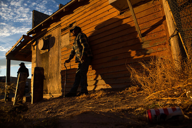 People stand beside a building as the sun sets over Whiteclay. Many of those who spend time drinking on the streets in Whiteclay spend their nights in a makeshift camp not far from the town.