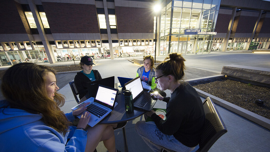 Four students study in the dusk light outside the Adele Hall Learning Commons.