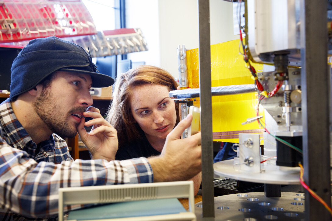 Mike Cox and Elizabeth Balerud watch as a lightweight boom and mock solar panel deploy from a space tool they helped build. 