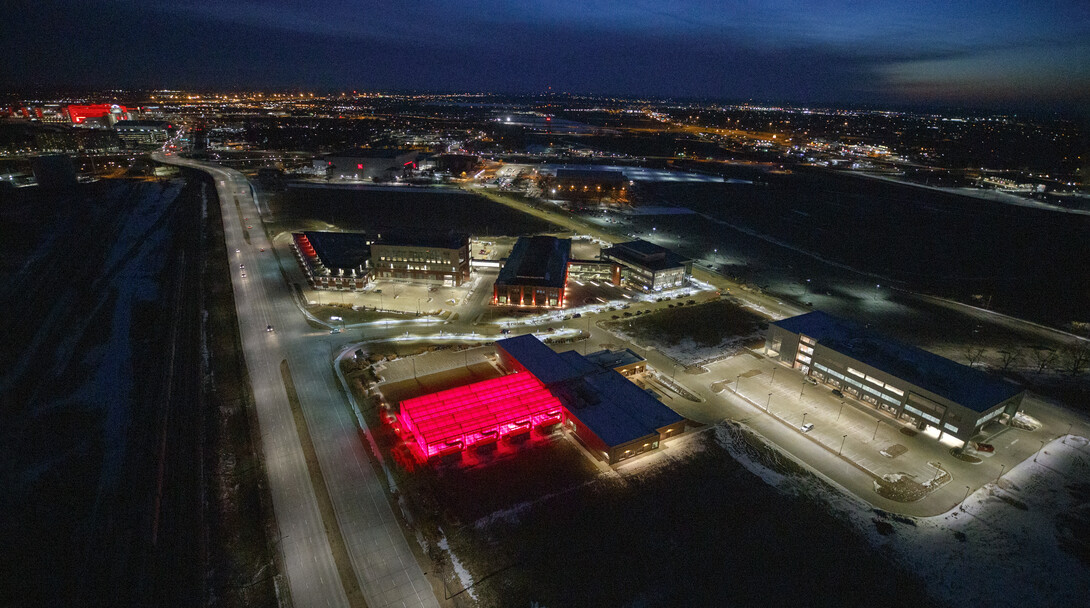 Greenhouses at Nebraska Innovation Campus glow red with Memorial Stadium and City Campus in the background.