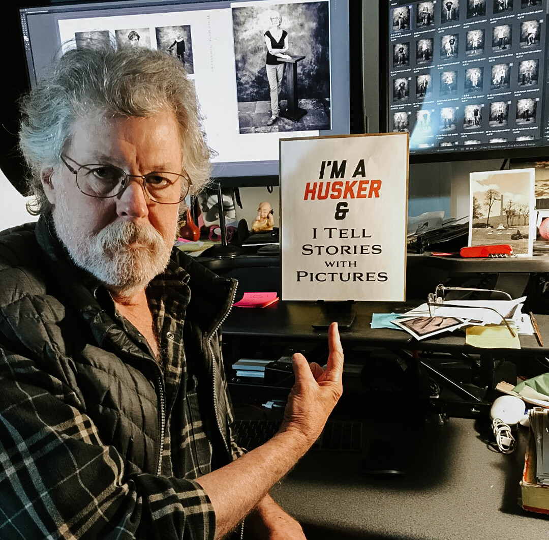 Portrait of Michael Farrell sitting in front of the computer he uses to edit photos.