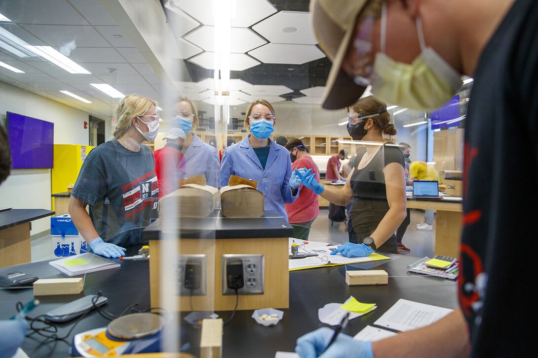 Sarah Brady, a chemistry lab teaching assistant (center, in blue), answers questions during a lesson in Hamilton Hall. Acrylic dividers are being used in the space to increase capacity of the lab space.