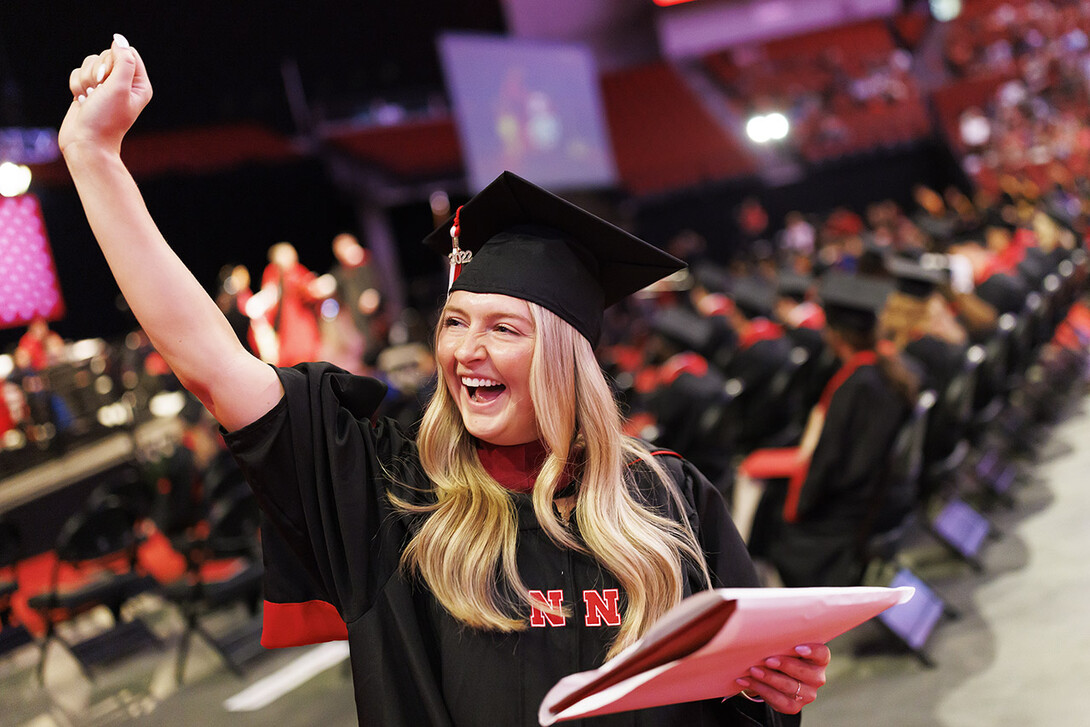 Natalie Henton, dressed in graduation attire, waves to family and friends after receiving her Master of Science in child, youth and family studies.