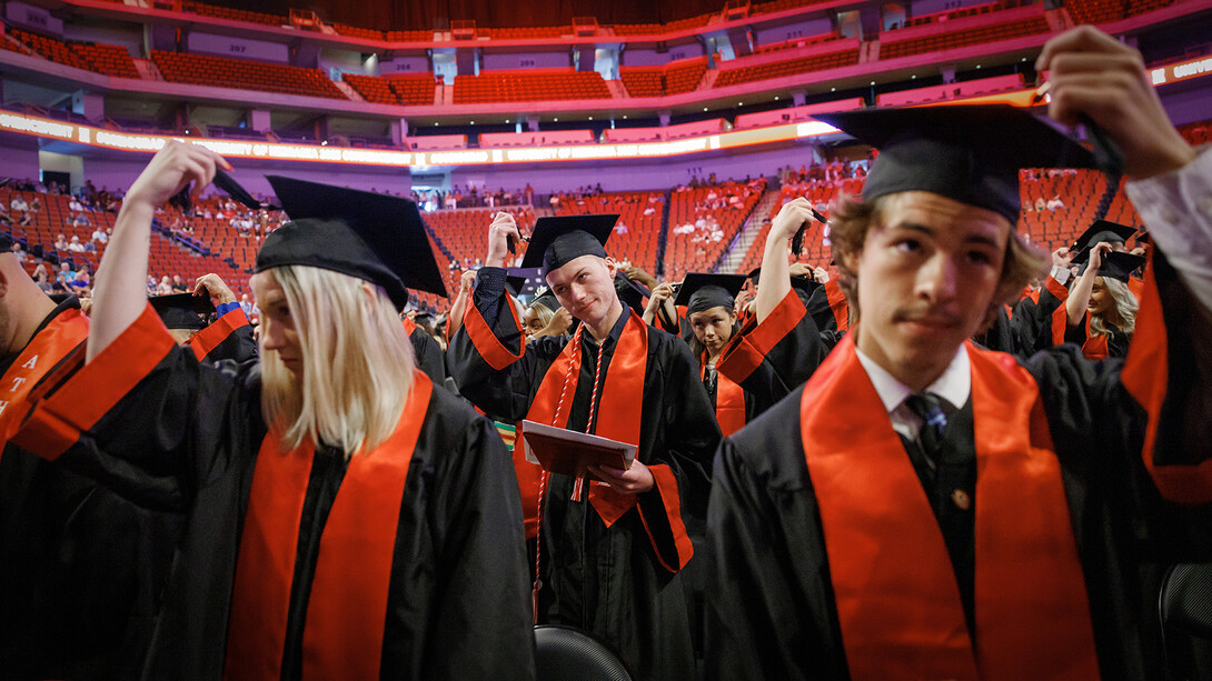 A group of graduates, with a young man at center, moves their tassels toward the end of the commencement ceremony.