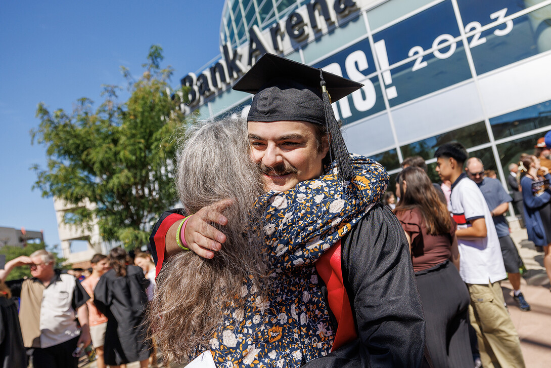 A young man in graduation regalia hugs an older woman outside of Pinnacle Bank Arena.