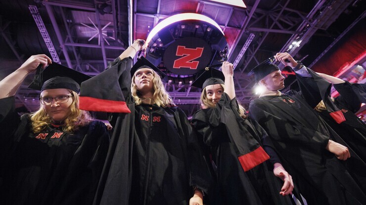 Four graduates — three young women and a young man — move the tassels on their caps at Pinnacle Bank Arena.