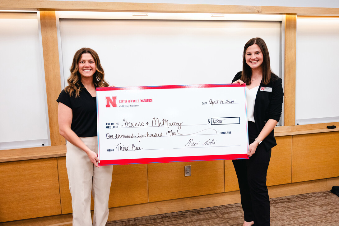 Two young women hold an oversized check for $1,500.