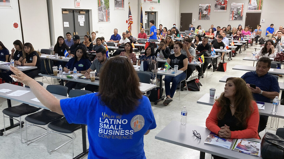 Sandra Barrera speaks in front of a crowd of a few dozen Latinx entrepreneurs, seated at tables.