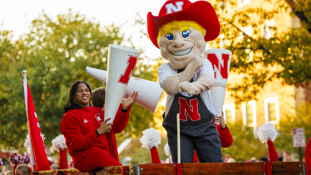 Herbie Husker and Spirit Squad member Amani Mfinanga cheer from a tractor-pulled wagon in the 2023 homecoming parade.