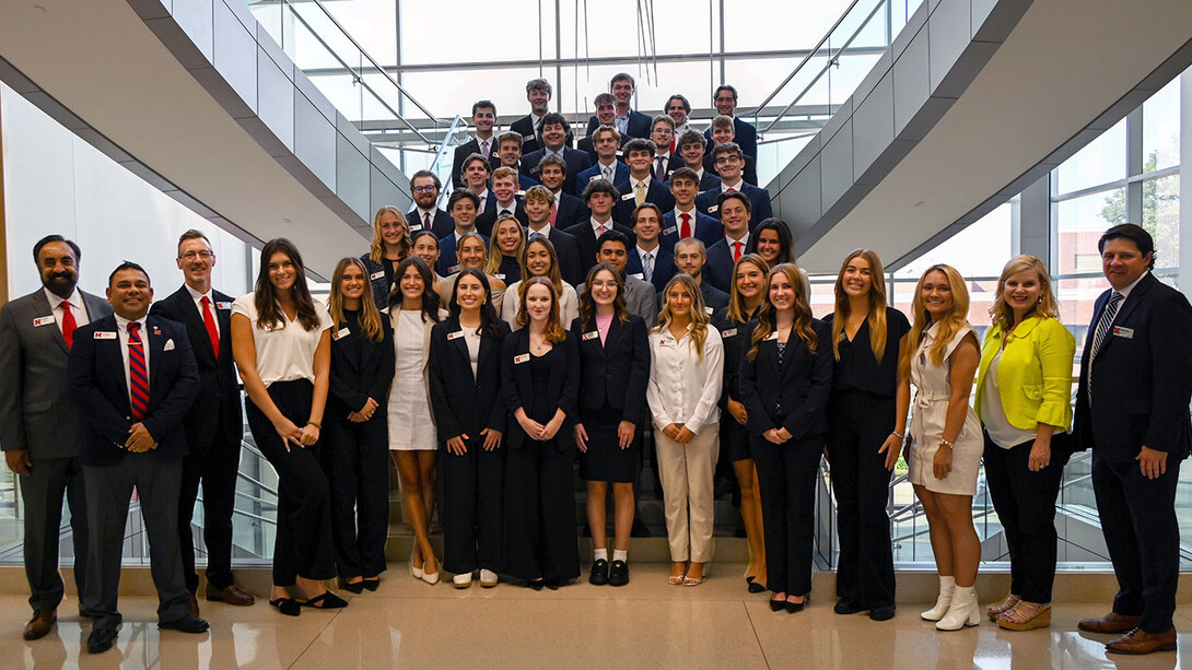 Students and faculty in formal attire pose on a staircase in Howard L. Hawks Hall.